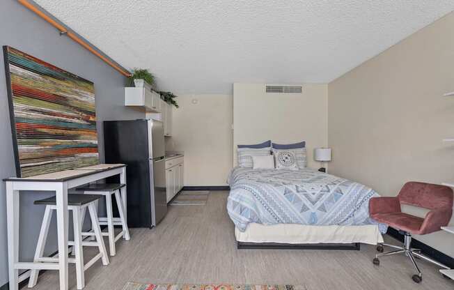 A bedroom with a bed, chair, and a fridge.