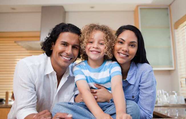 A family of three is sitting together in a kitchen.