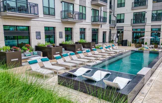 an outdoor pool with lounge chairs and umbrellas in front of an apartment building