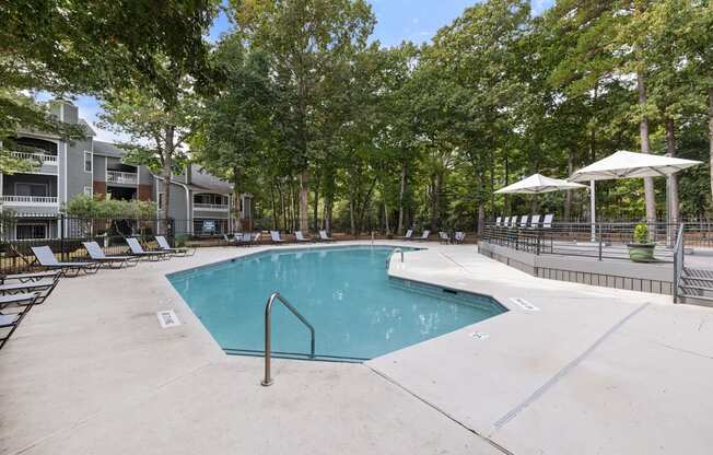 A swimming pool surrounded by trees and chairs.