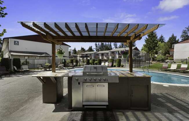 Decadent Resident Outdoor Kitchen with a Shaded Wooden Pergola Next to the Sparkling Swimming Pool at Pinewood Square Apartment Homes, Lynnwood, WA