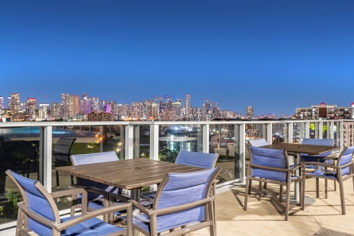 a rooftop terrace with tables and chairs overlooking a city at night