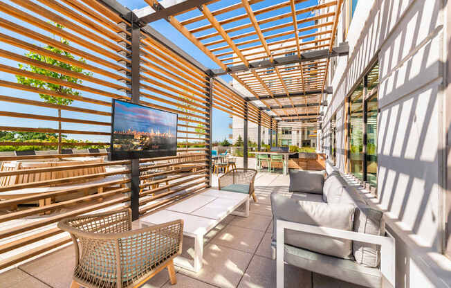 A patio with a white couch, a wicker chair, and a flat screen TV.