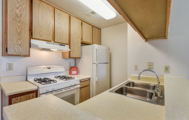 Vacant apartment kitchen with al lot of cabinet storage, white stove and refrigerator. 