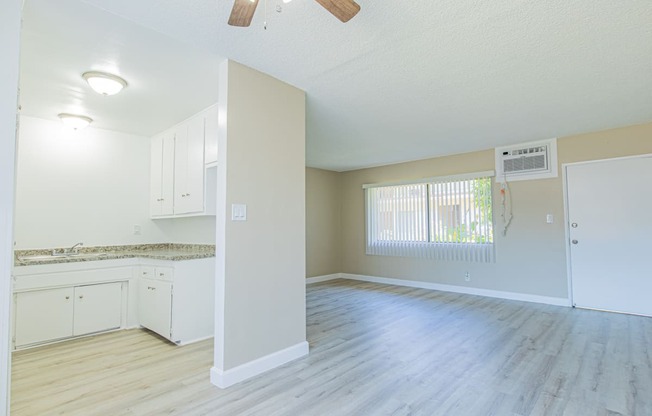 an empty living room and kitchen with white cabinets and wood floors