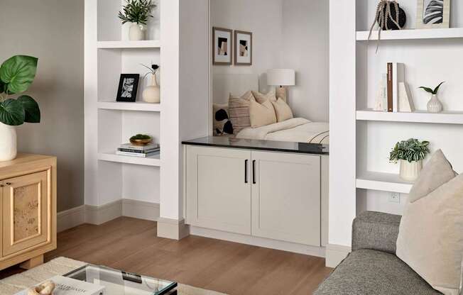 A living room with a grey sofa, a wooden cabinet, and a white shelf with decorative items.