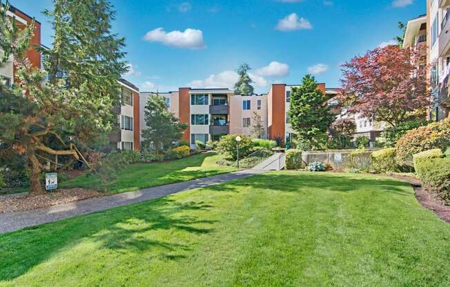 A beautiful exterior here at Watercrest with lush green lawns, landscaped trees, and a paved walking path, leading to well-maintained apartment buildings with private balconies, creating a peaceful and park-like community setting.