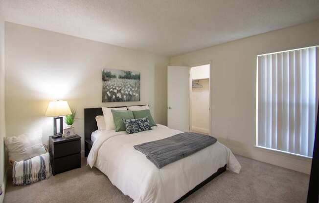 A bedroom with a large bed and a painting on the wall in a 515 square foot 1 bedroom, 1 bath apartment home at Canyon Creek Apartments in Dallas Midtown neighborhood of Dallas, TX.