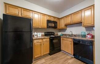 A black refrigerator stands in a kitchen with wooden cabinets and black appliances.