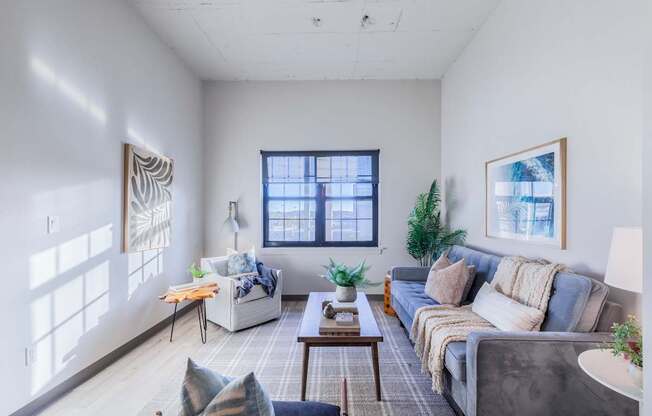 A living room with a grey couch, a white chair, a coffee table, and a window with a view of the city.