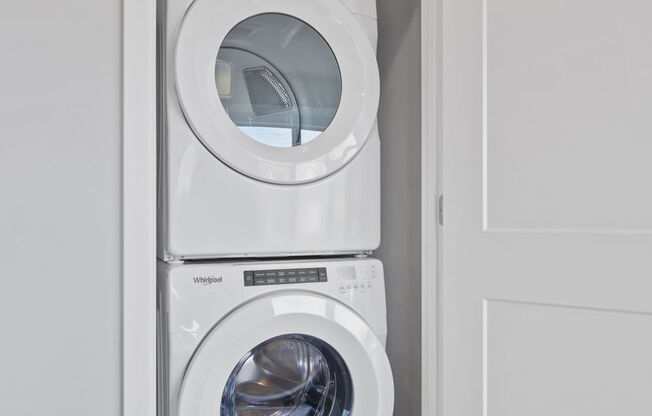 A white washing machine is stacked on top of another white washing machine in a small laundry room.
