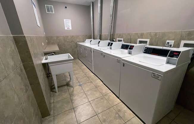 a laundry room with four washing machines and three sinks