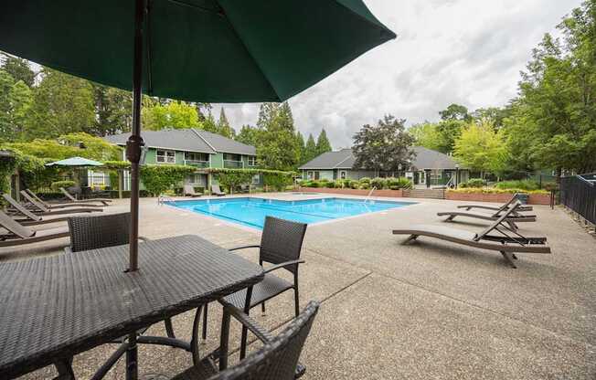 A pool area with a table and chairs and a green umbrella.