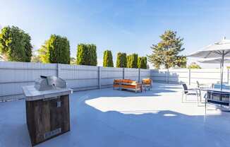 Outdoor lounge with umbrella-covered tables, gas BBQ, and an oversized orange patio couch and coffee table.at The Lakes Apartments, Moses Lake, WA