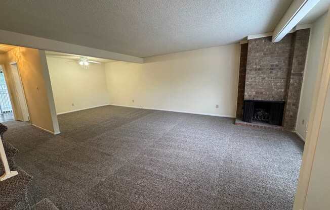 A large, empty room with a fireplace and a carpeted floor.