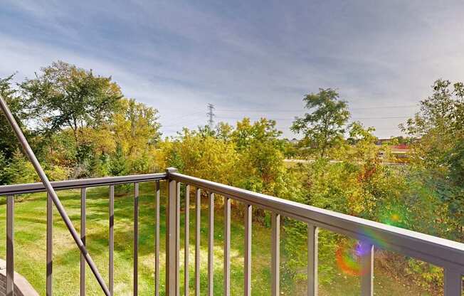 A balcony with a metal railing overlooks a green lawn and trees.