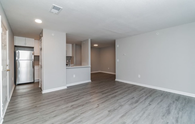 an empty living room and kitchen with a refrigerator and