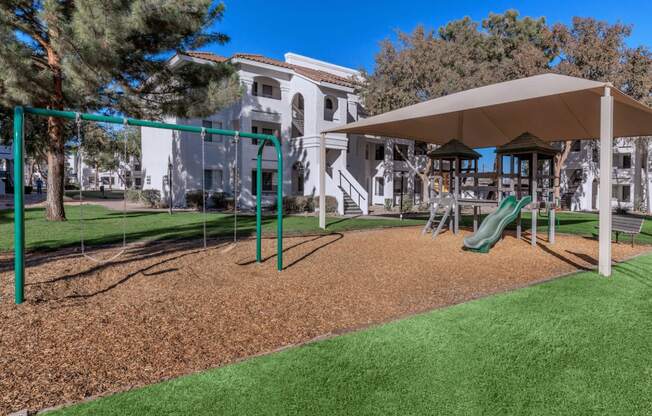 a playground with a slide and swings in front of a building