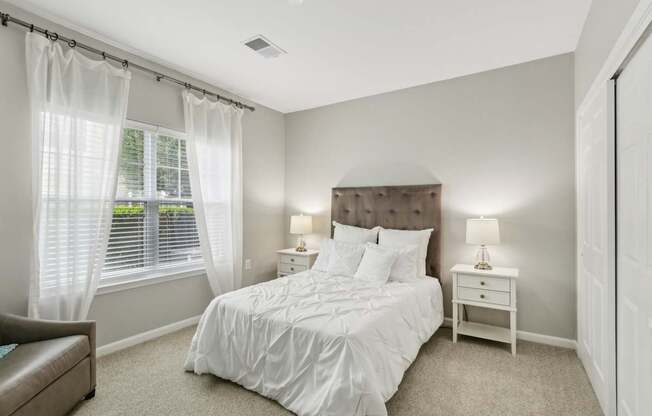 A bedroom with a large bed, two nightstands, and a window with curtains.