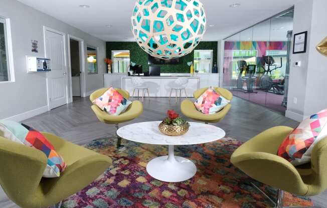 Fusion Las Vegas apartments lobby sitting area with four green chairs and geometric throw pillows around a round coffee table and modern light fixture.