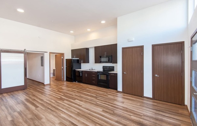 an empty living room with wood flooring and a kitchen