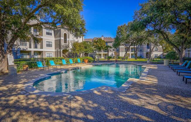A swimming pool near the clubhouse at Saxony at Chase Oaks Apartments in Dallas, TX, with lounge chairs, lush trees, and landscaped surroundings.