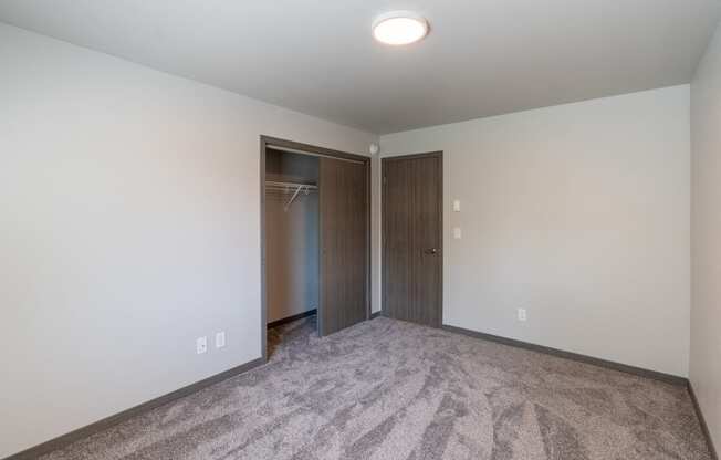 A bedroom with carpet and a door to a closet. Fargo, ND Granger Court Apartments.