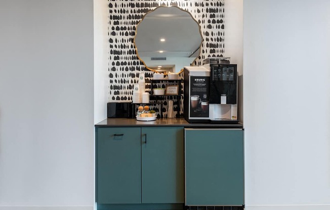 a coffee bar with green cabinets and a mirror on the wall