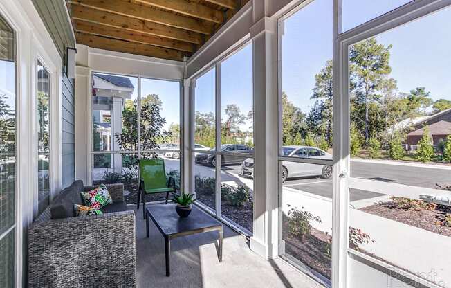 a covered porch with a couch and a coffee table and large windows