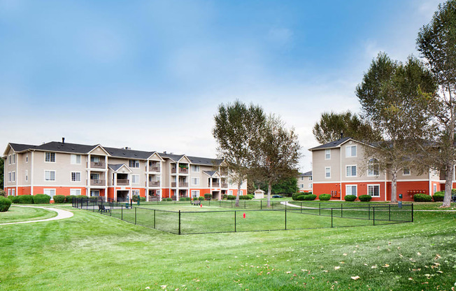 Ardenne Apartments grassy, fenced in dog park with community buildings behind it.