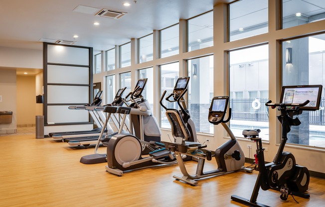 a gym with cardio equipment and large windows