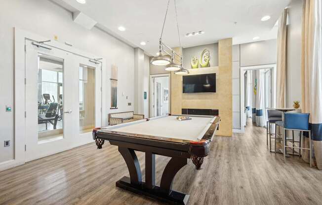 A pool table is in the middle of a room with a television and a bar.