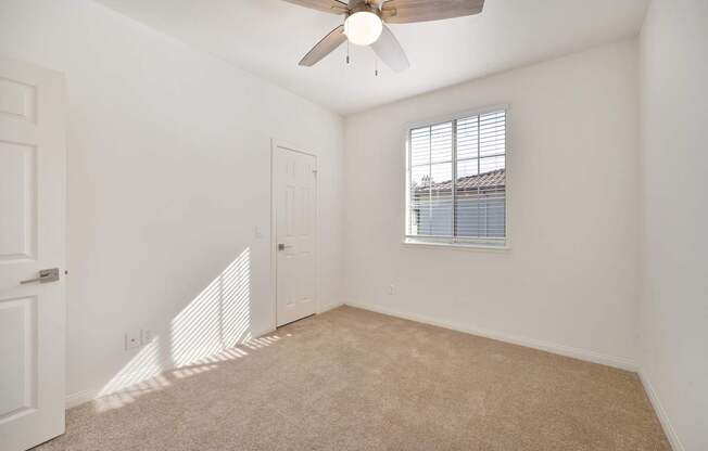 A room with a ceiling fan and a window with blinds.