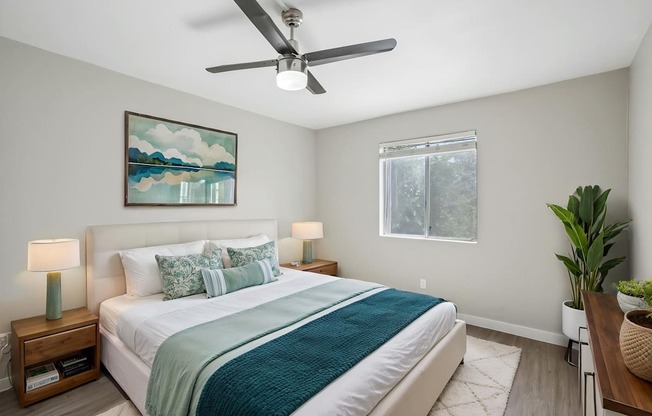 A bedroom with a bed, a ceiling fan, and a painting on the wall.