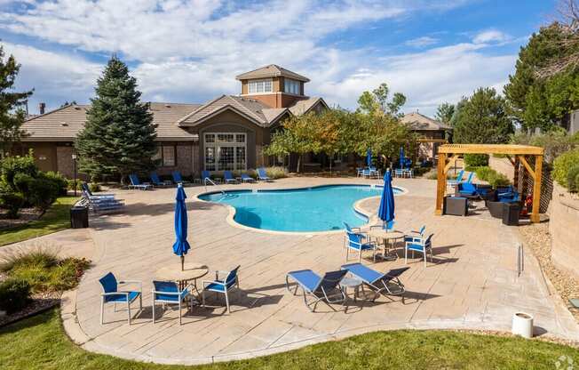 a pool with blue chairs and umbrellas and a house with a swimming pool
