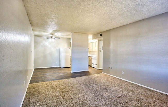 an empty living room with a ceiling fan and a kitchen