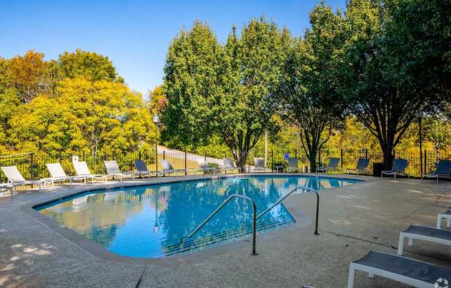 a swimming pool with chairs around it and trees in the background