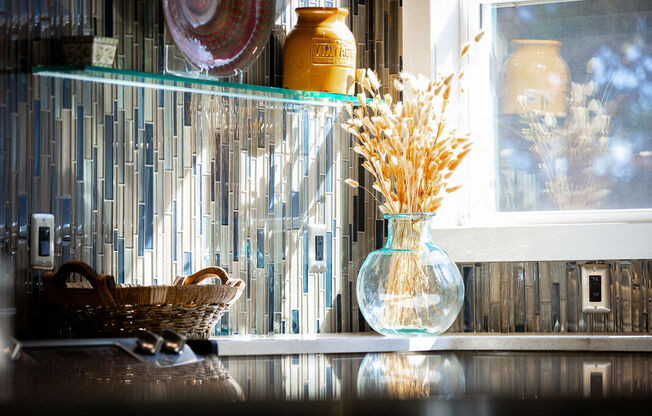 a glass vase with flowers on a counter next to a window