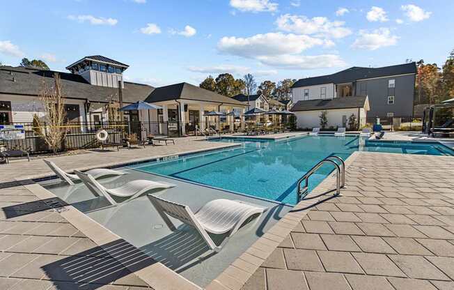 A large swimming pool with sun loungers and a building in the background.