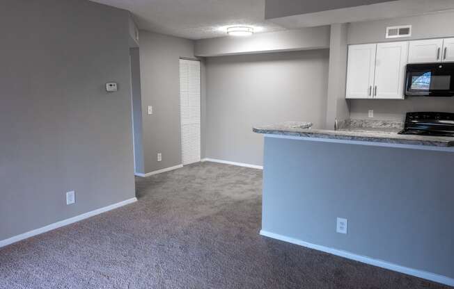 an empty living room with a kitchen and a counter top