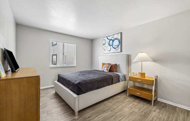 A bedroom with a bed, nightstand, and a painting on the wall.