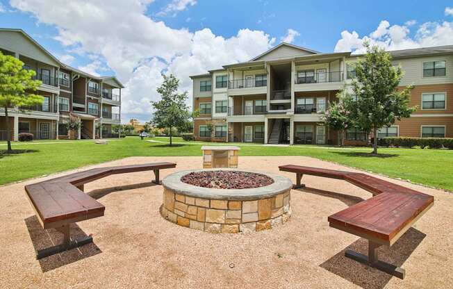 A fire pit sits in the middle of a gravel area with benches on each side.