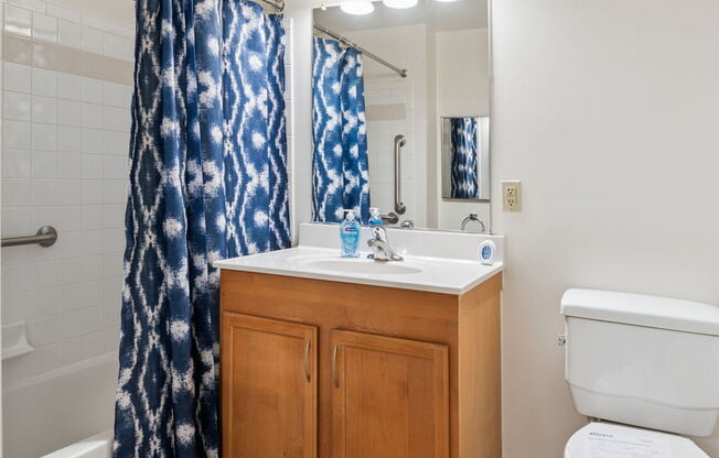 A bathroom with a white toilet, a sink with a wooden cabinet, and a blue shower curtain.