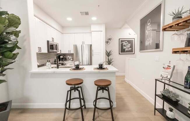 A kitchen with white cabinets and a white countertop with two stools in front of it.