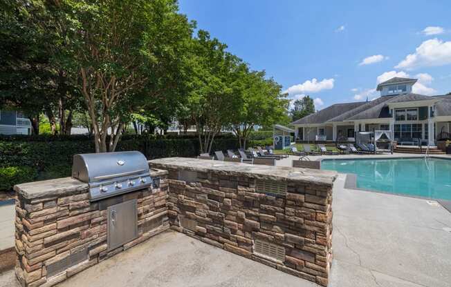 a barbecue grill next to a swimming pool with a house in the background