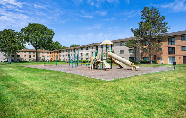 A playground with a slide and swings in front of a building.