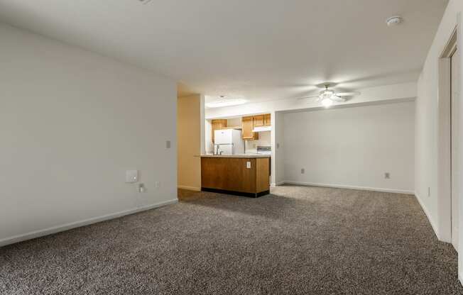 an empty living room with carpet and a kitchen in the background at Pheasant Run in Lafayette, IN 47909