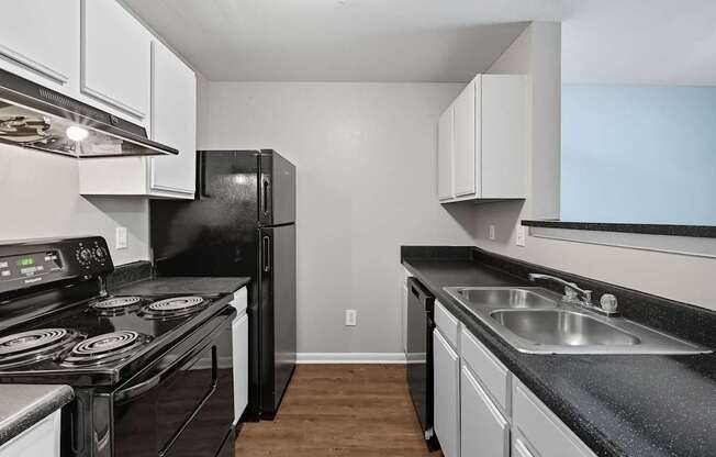 A black refrigerator sits in a kitchen with white cabinets.