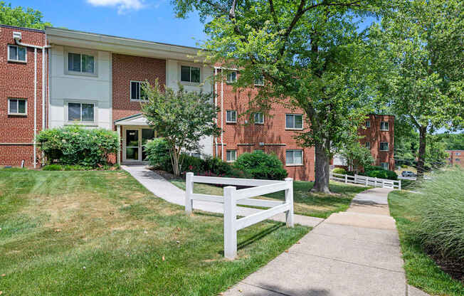 A white picket fence separates a grassy area from a brick building.