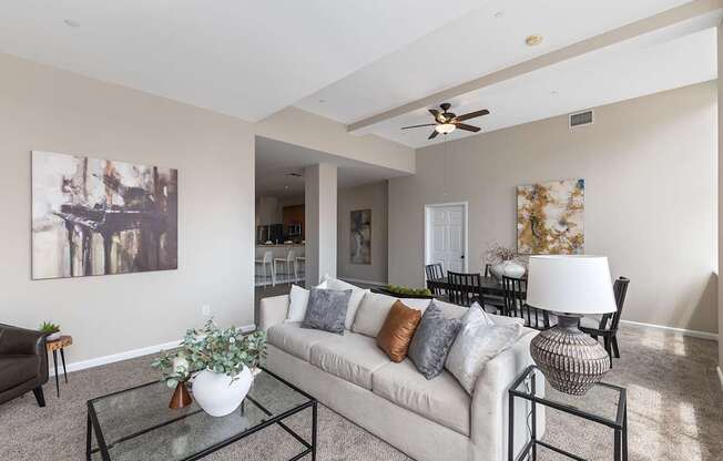 A living room with a white couch, a glass coffee table, and a painting on the wall.
